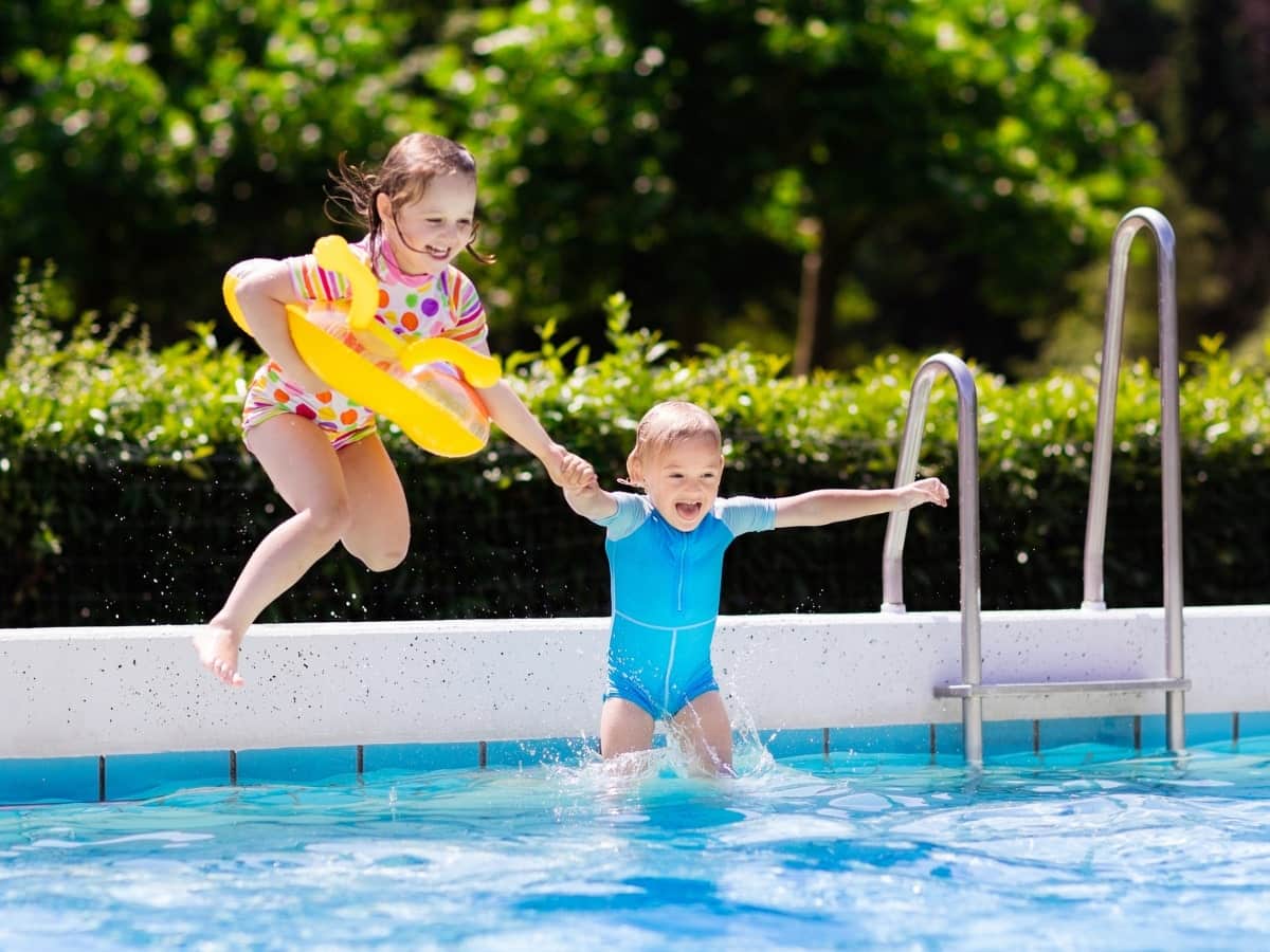 Two children jumping into a swimming pool, highlighting the importance of stringent pool fence regulations for safety in Australian swimming pools.