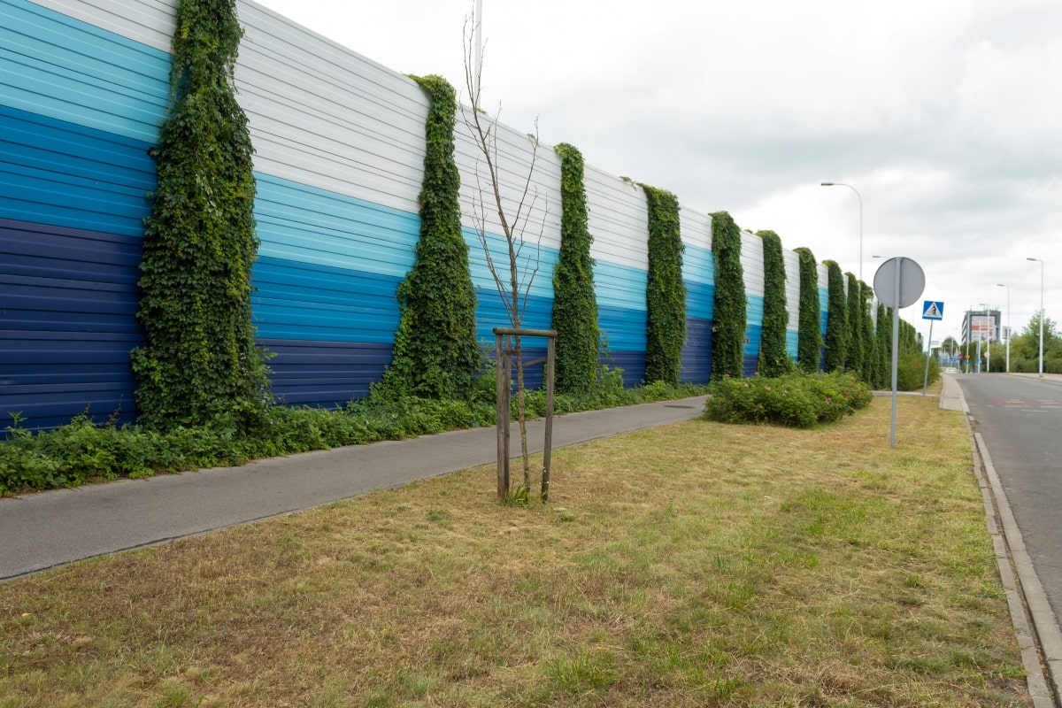 A colourful acoustic fence next to a road, designed to reduce traffic noise.