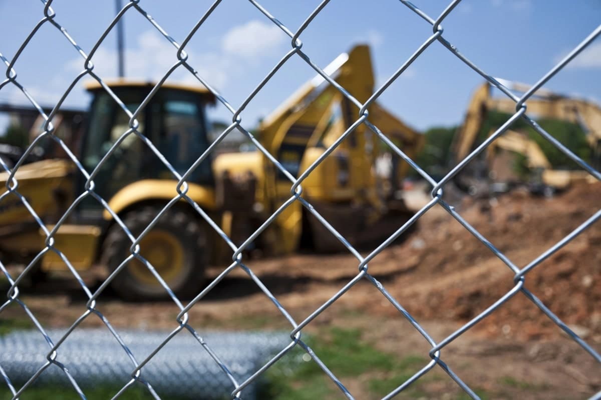 A close-up of a chain link fence with machinery in the background.