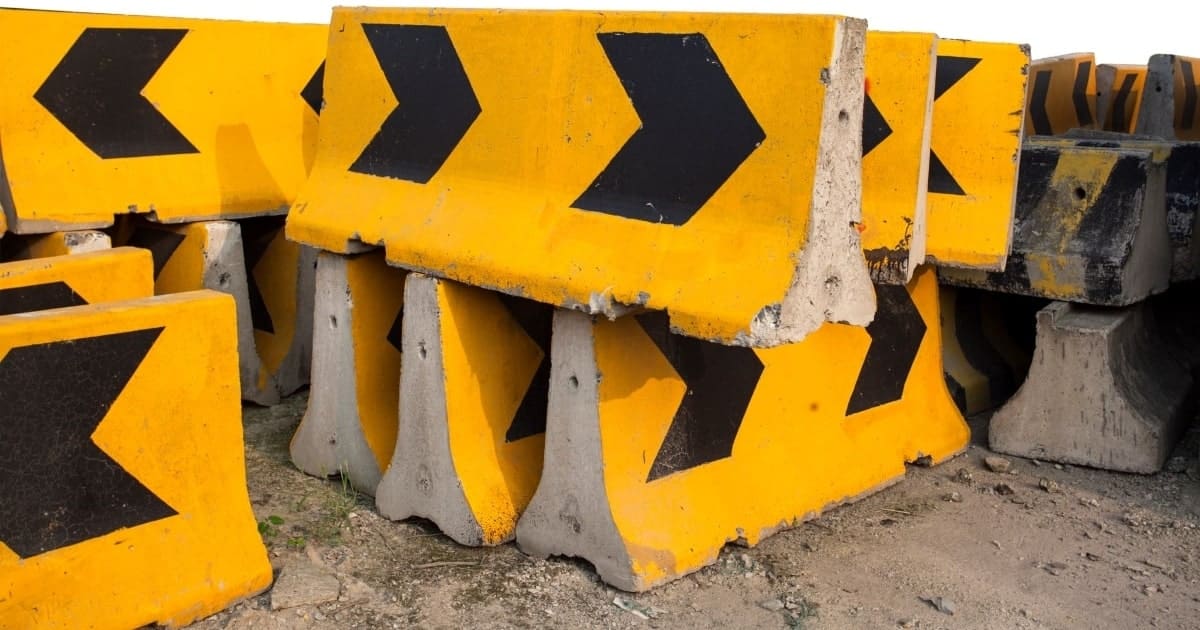 Stacked concrete road barriers, painted bright yellow and black.