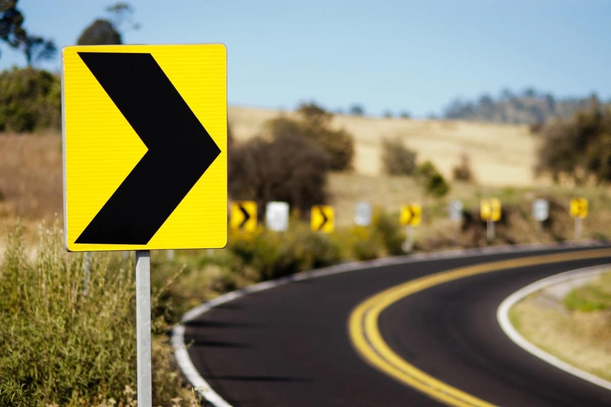 A yellow and black sign on the side of the road, indicating a bend in the road.