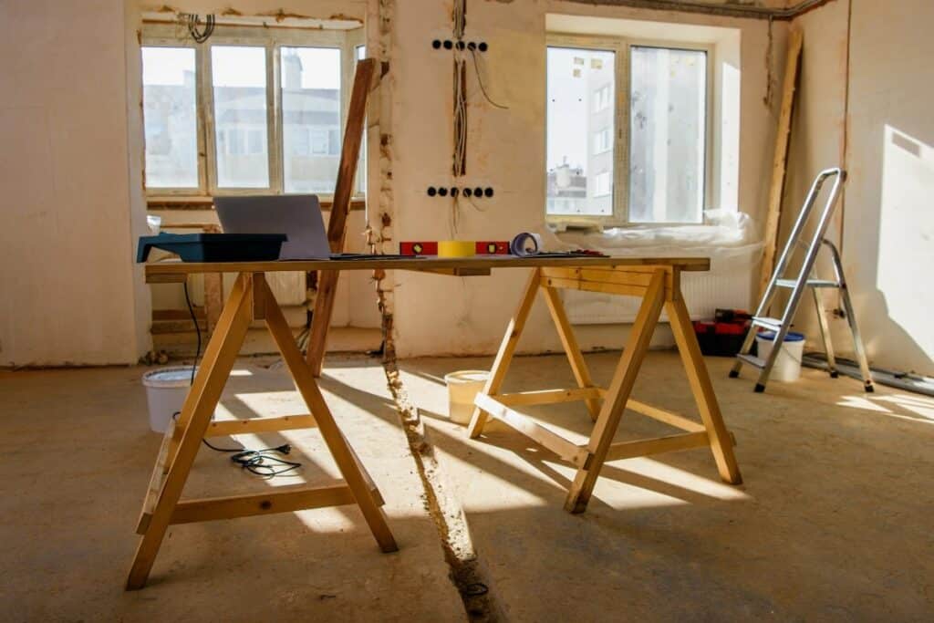 Interior view of a renovation site with trestle scaffolding supporting a makeshift work table, surrounded by construction tools and materials.