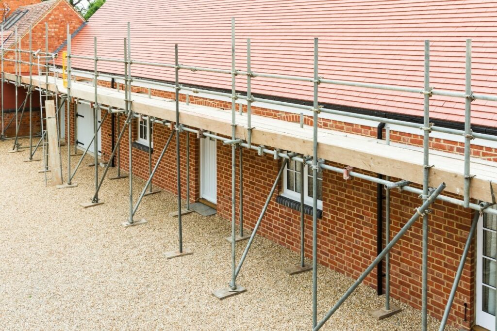 Single scaffolding system erected alongside a brick building with a tiled roof, providing essential support for construction or renovation work.