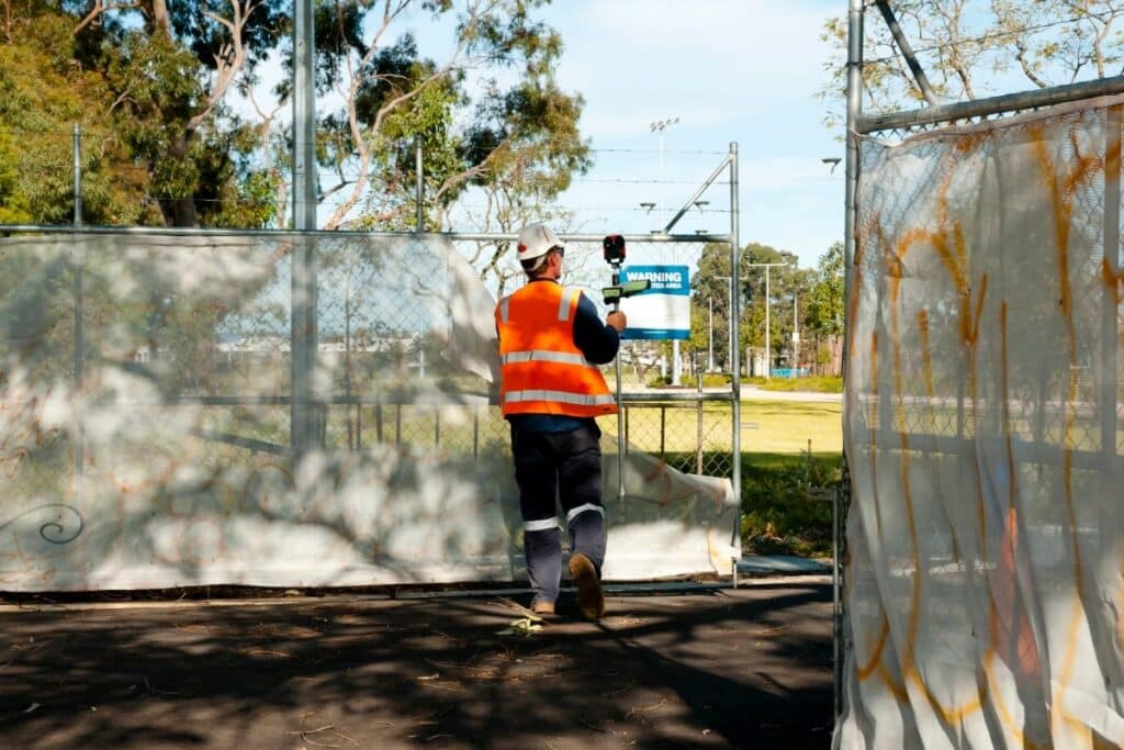 Surveyor in hi-vis walking through construction site with temporary fencing.