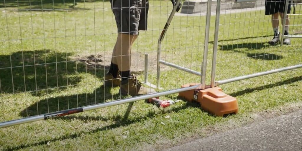 Person in work boots installing a temporary fence on a rental property, highlighting the convenience of non-permanent fencing options.