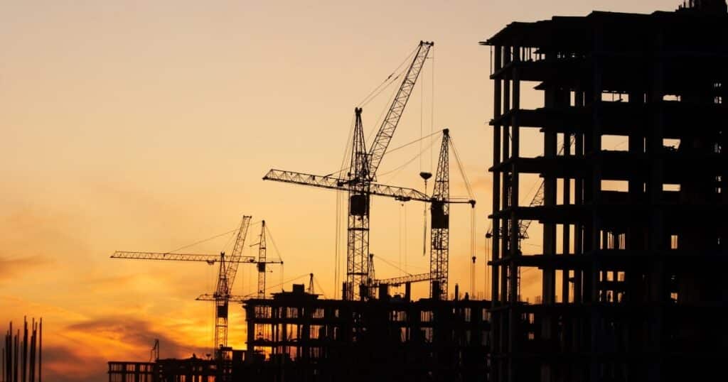 A construction site with buildings and cranes, silhouetted against the sky at sunset.