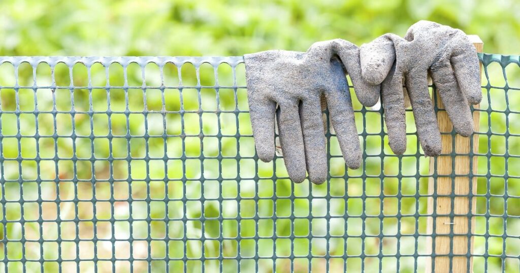 Close-up of a plastic mesh fence with a pair of work gloves draped over it, illustrating an easy-to-install temporary fencing for renters.